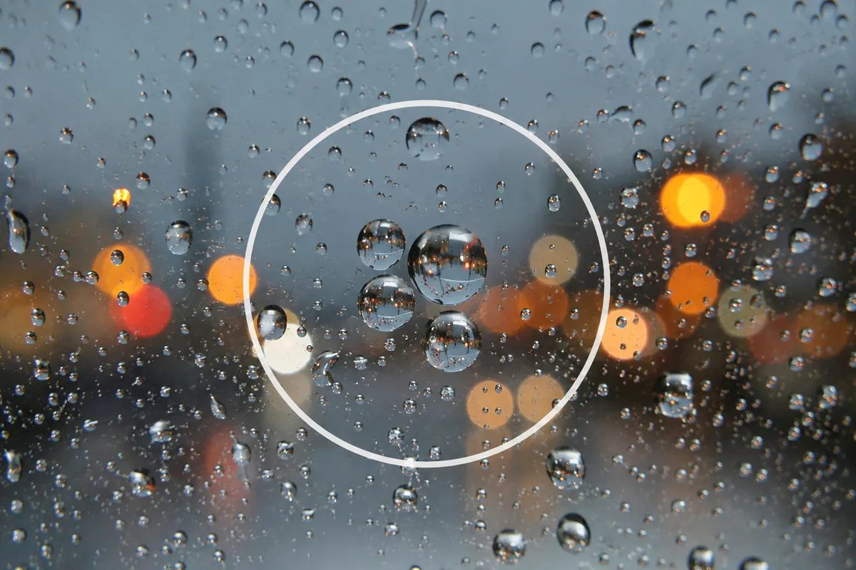 雨の日の作例。窓ガラスの水滴にピントを合わせ、奥の街をぼかして主役を水滴にした構図イメージ。
